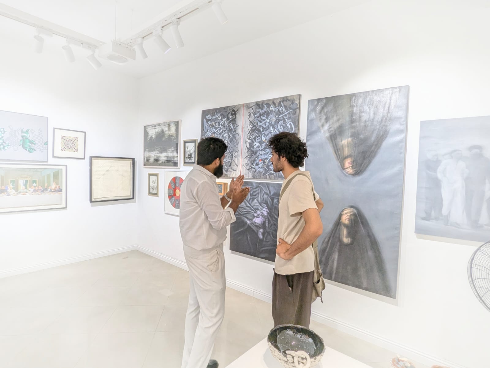 Khuzaima Ayaz speaking with a visitor beside the exhibited calligraphic work